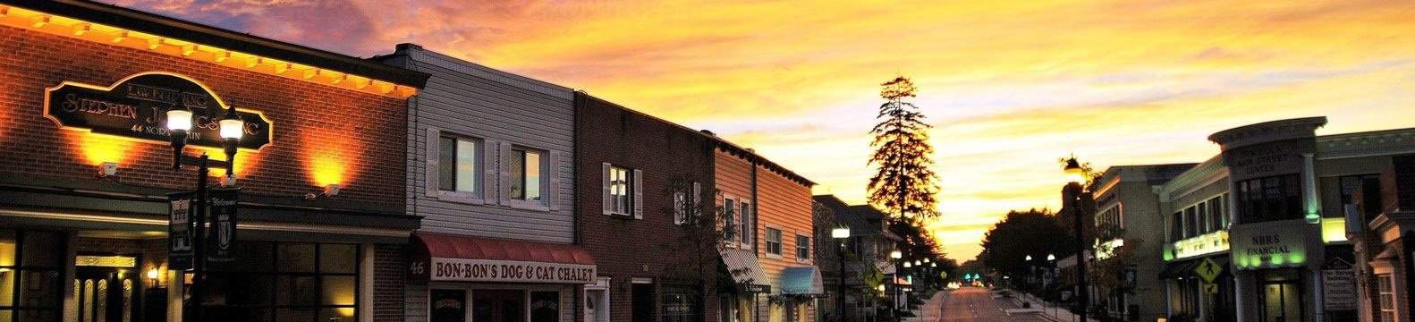 Small-town main street with lit storefronts at golden sunset.