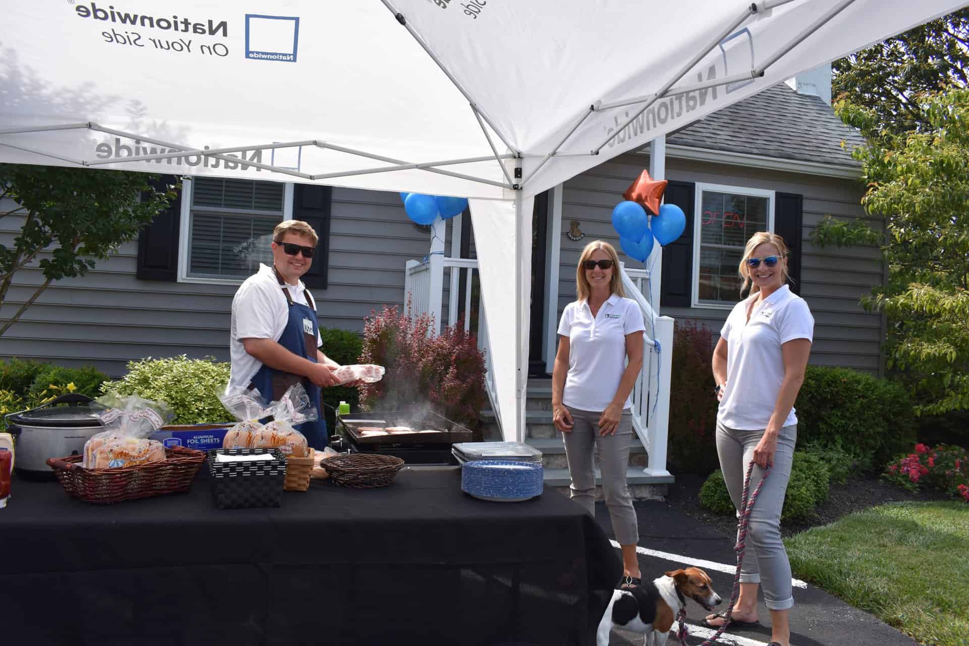 Three Gerety Insurance employees at a tented grill station, woman holding small dog.