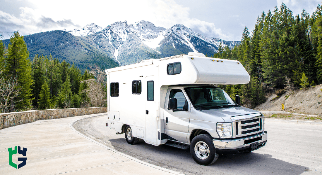 White RV parked on mountain road with snow-capped peaks