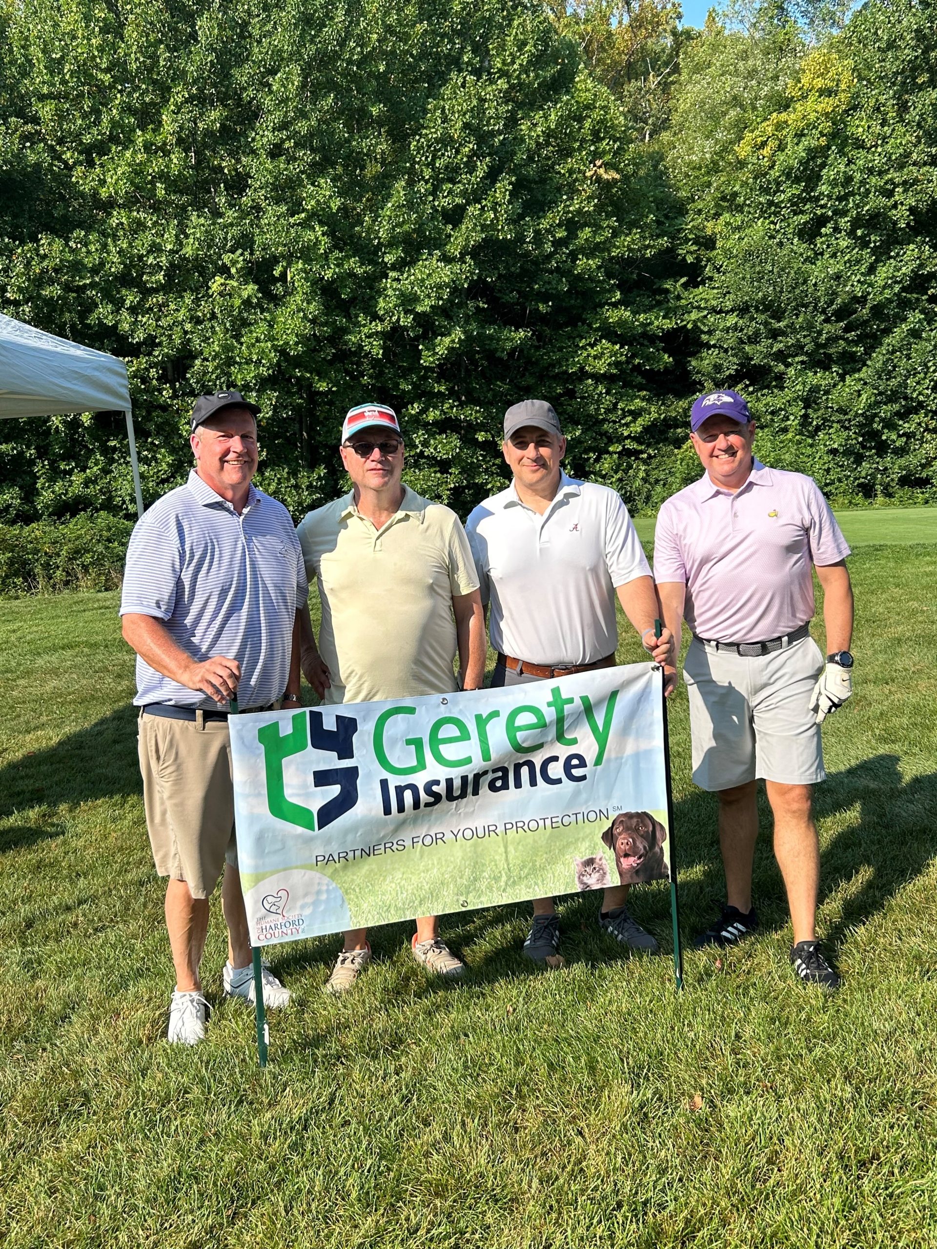 Four golfers stand behind a Gerety Insurance banner on grass.