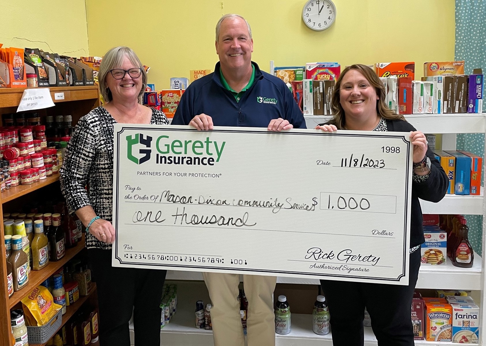 Three people holding large $1,000 Gerety Insurance check in pantry