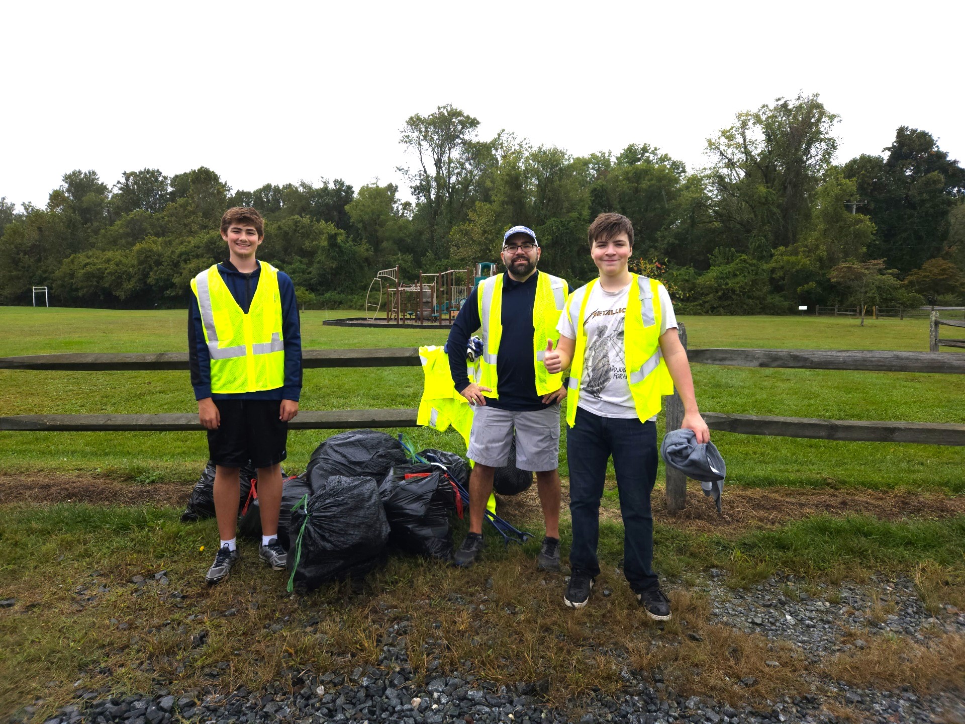 Three volunteers in yellow safety vests with collected trash bags