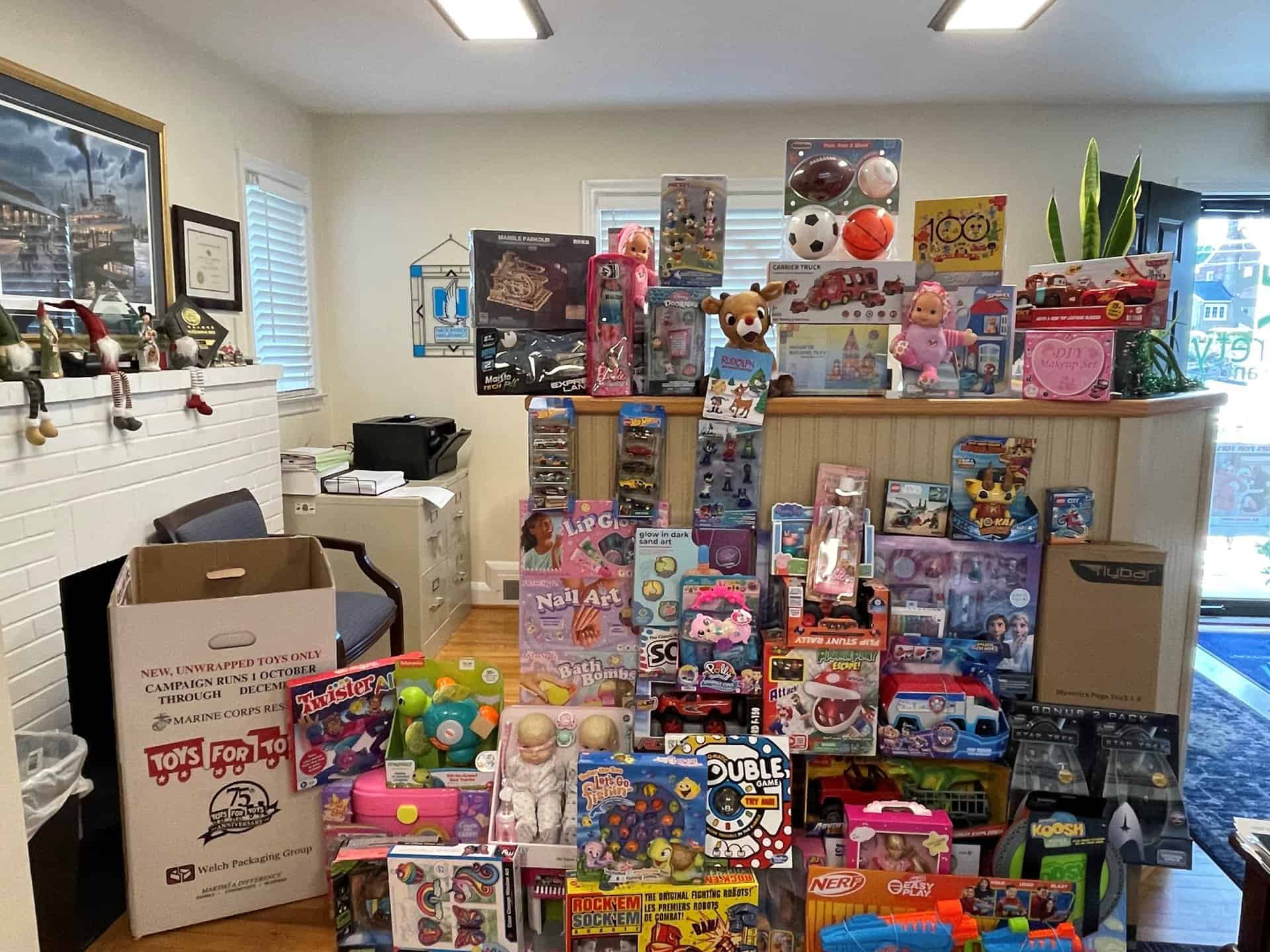 Stack of assorted new children's toys and a Toys for Tots donation box