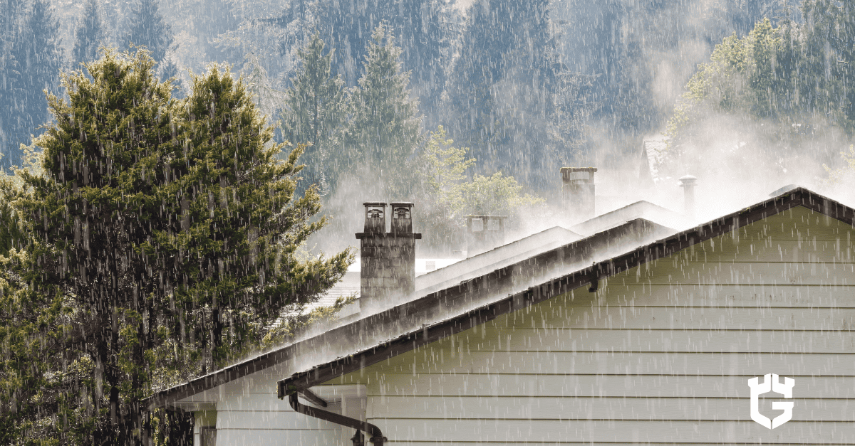 Rain-soaked house roofs and chimneys with misty trees behind