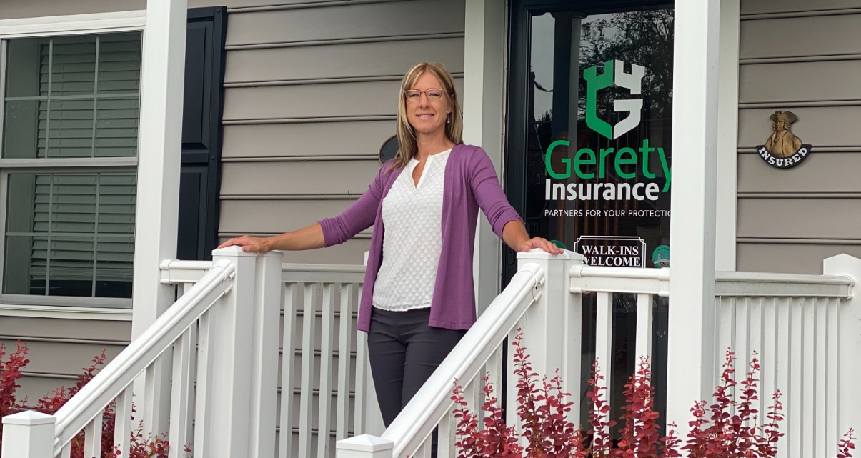 Woman in purple cardigan stands on a porch outside Gerety Insurance.