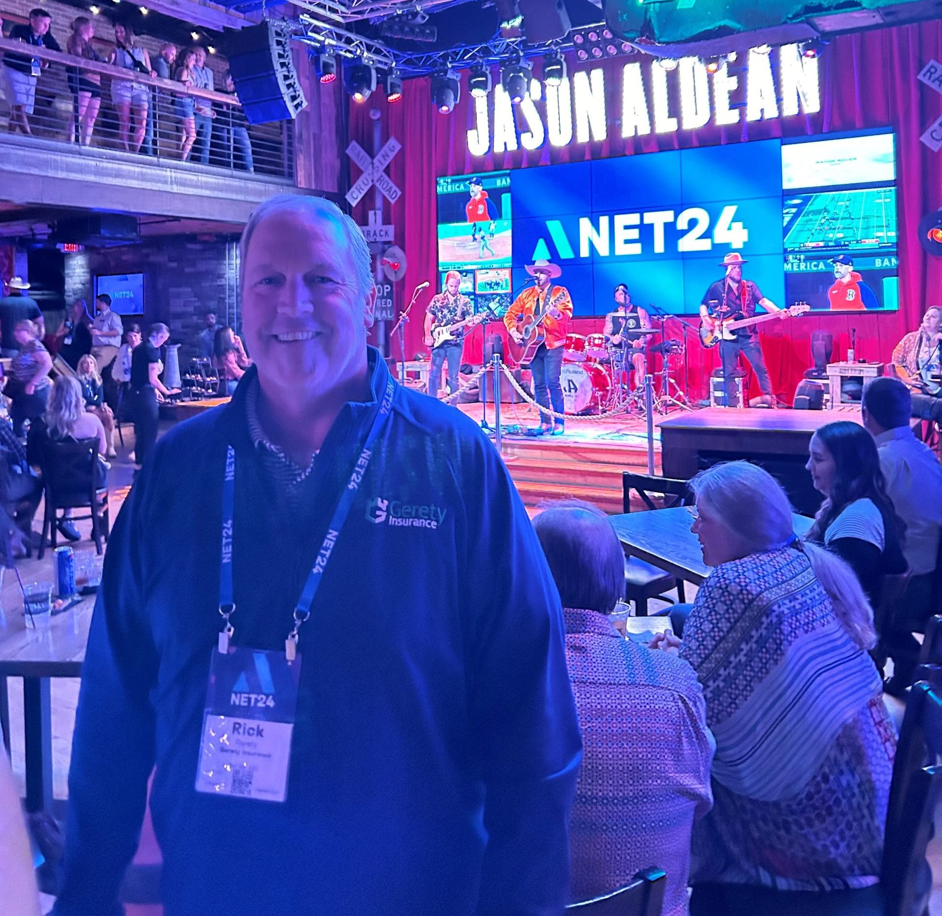 Smiling Rick Gerety in front of band on stage with Jason Aldean sign