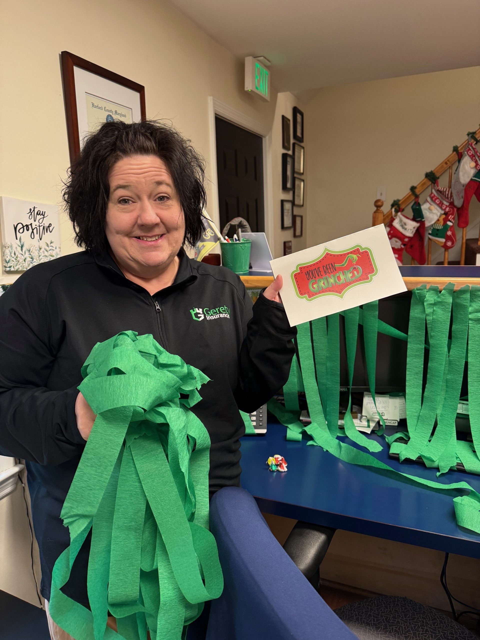 Woman holding green streamers and a You've Been Grinched card