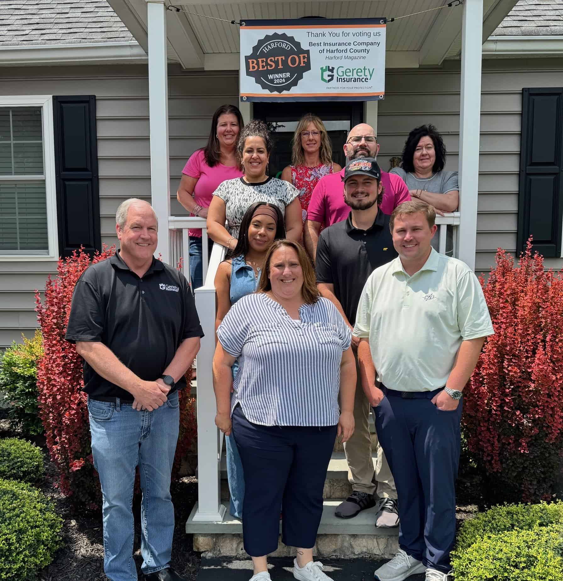 Group of smiling Gerety staff on porch under award banner
