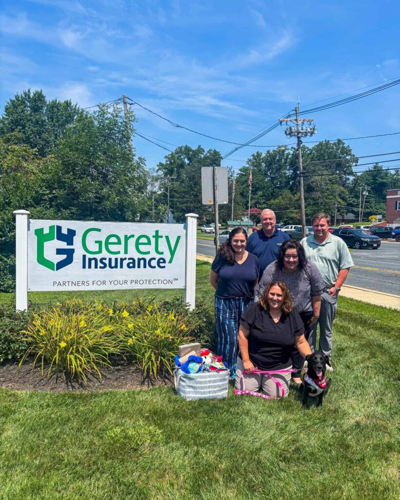 Gerety Insurance staff group with a black dog posing beside outdoor sign