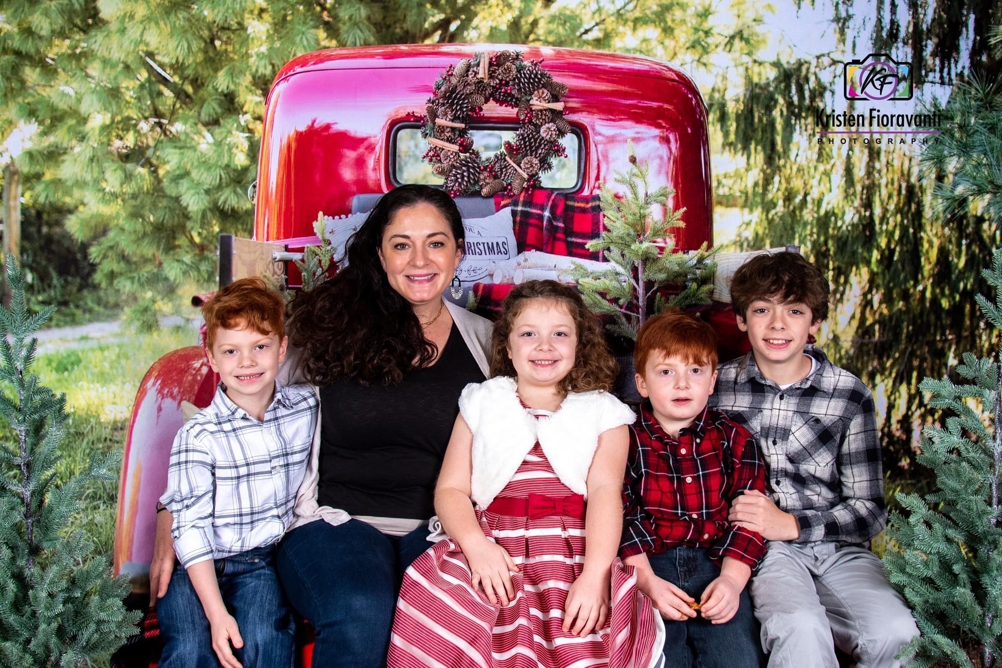Amy Green seated with four children in a holiday-themed portrait in front of a red vintage truck and Christmas decorations.