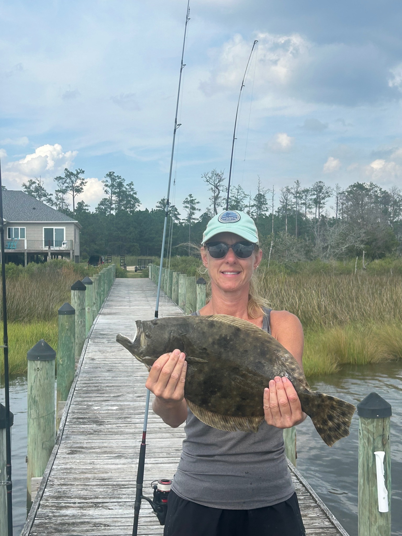 Cindy Dotson holding a flat fish on a wooden dock with fishing rods in the background.