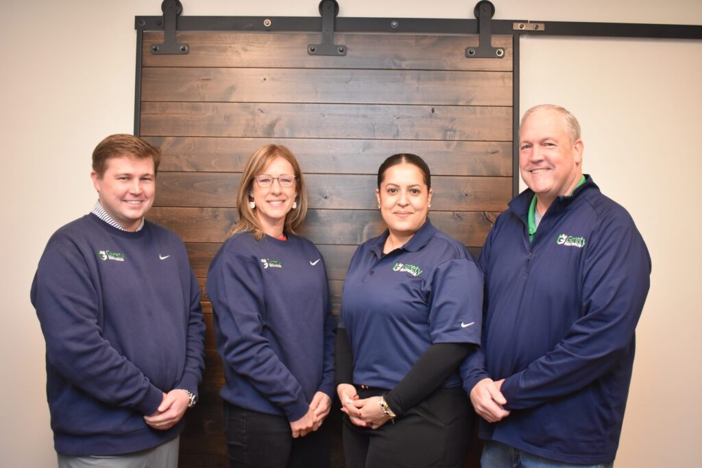 Four smiling Gerety employees in navy branded shirts standing before a wooden wall