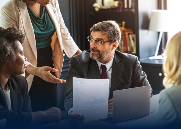 Business meeting: man in suit, glasses, holding report while colleagues listen