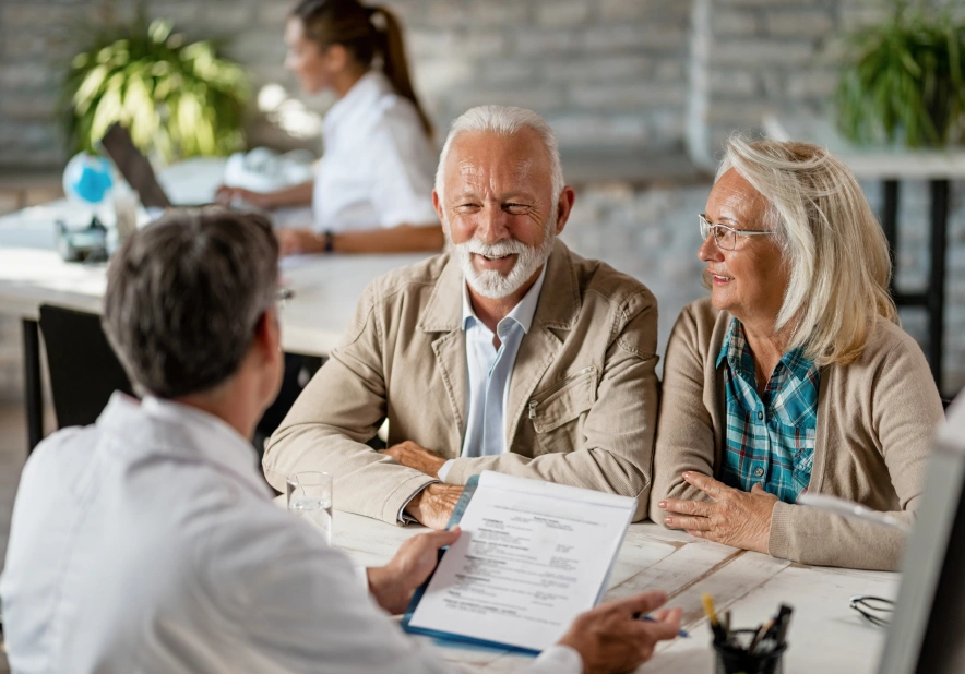 Smiling elderly couple meets a professional at a desk, reviewing documents.