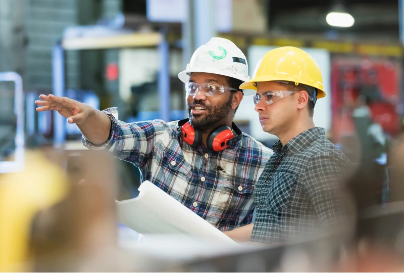 Two workers in hard hats and safety glasses reviewing plans