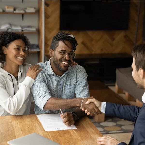 Smiling couple with insurance agent signing papers and shaking hands