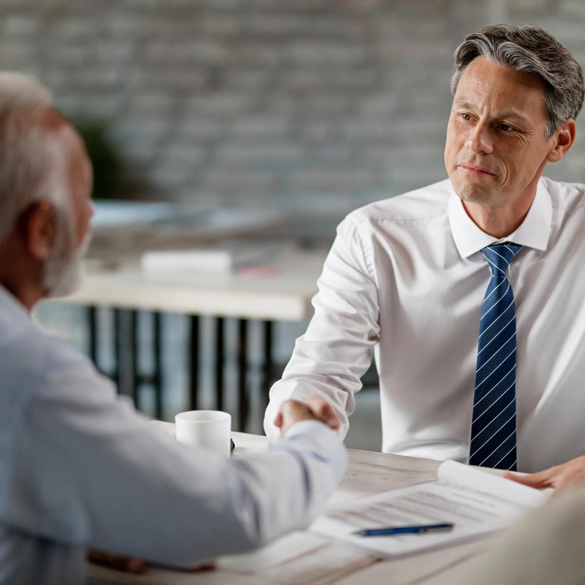 Two men shaking hands across a table with documents in a professional setting