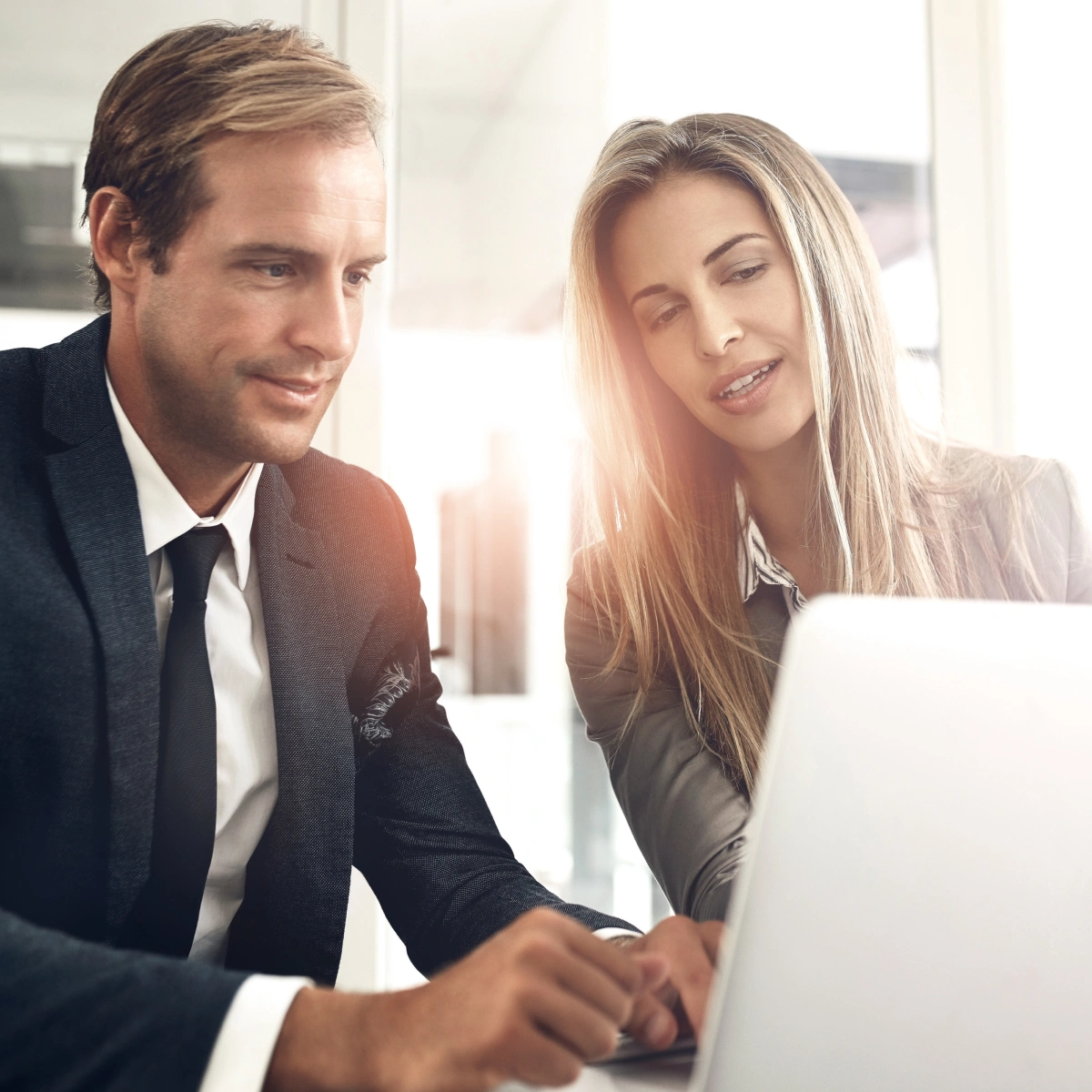 Two business professionals working together on a laptop in a bright office setting