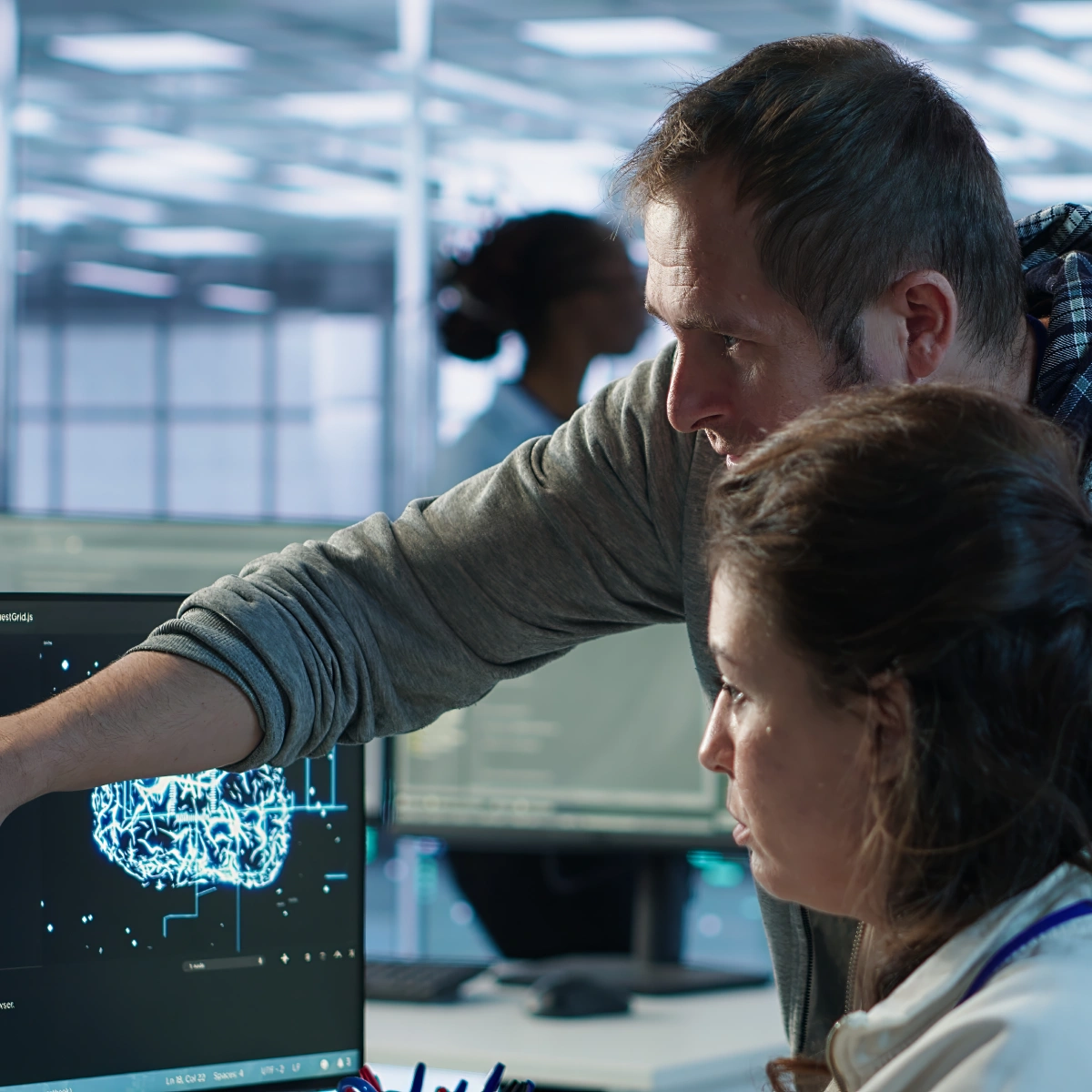 Man and woman analyzing digital brain model on a computer screen in an office setting.