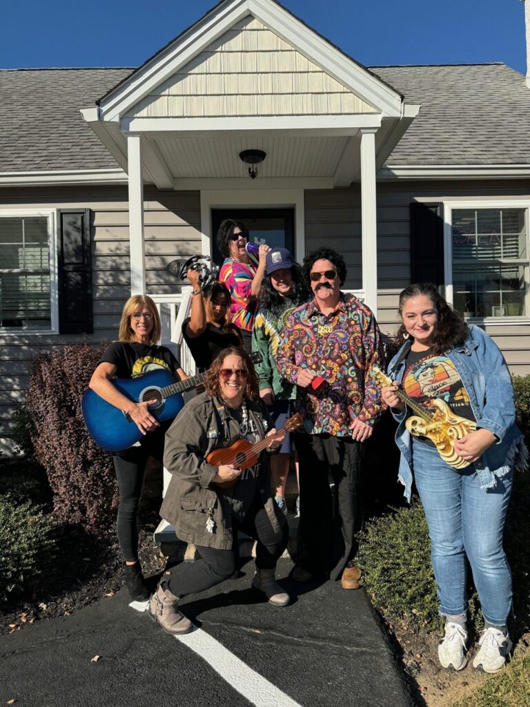 Seven people in colorful 1970s outfits holding instruments on a porch